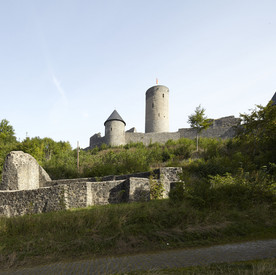 Ruine Nürburg zwischen Bäumen im Hintergrund, davor die Reste einer Burgkapelle