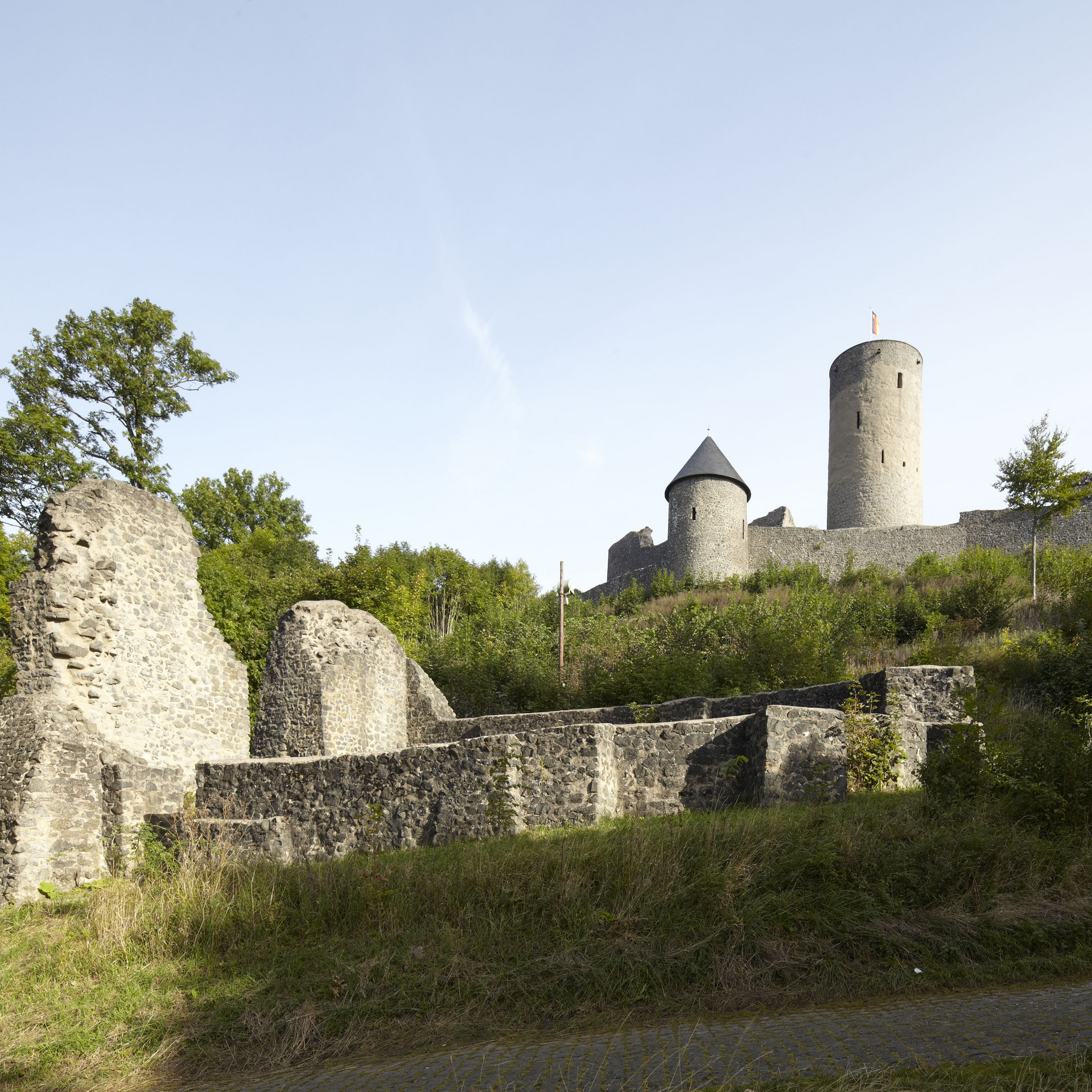 Ruine Nürburg zwischen Bäumen im Hintergrund, davor die Reste einer Burgkapelle