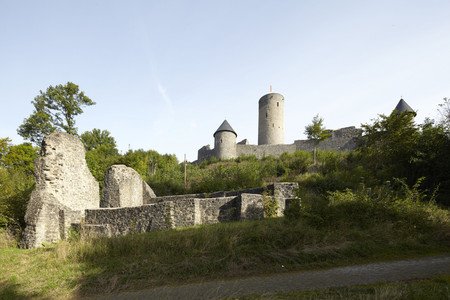 Ruine Nürburg zwischen Bäumen im Hintergrund, davor die Reste einer Burgkapelle