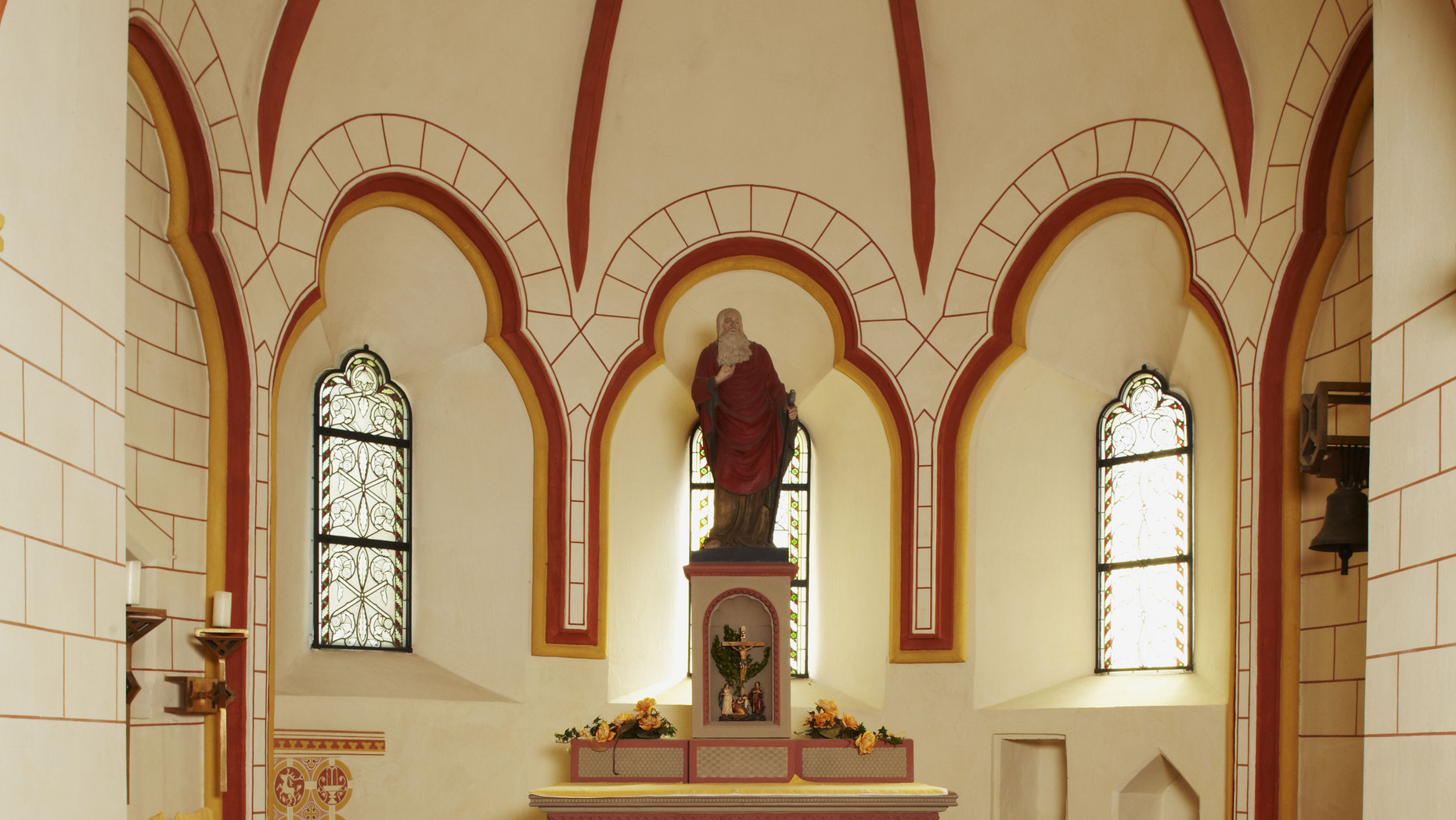 Blick in den Chor mit Glocke, Bank, Stühlen, Kerzen und zentralem Altar
